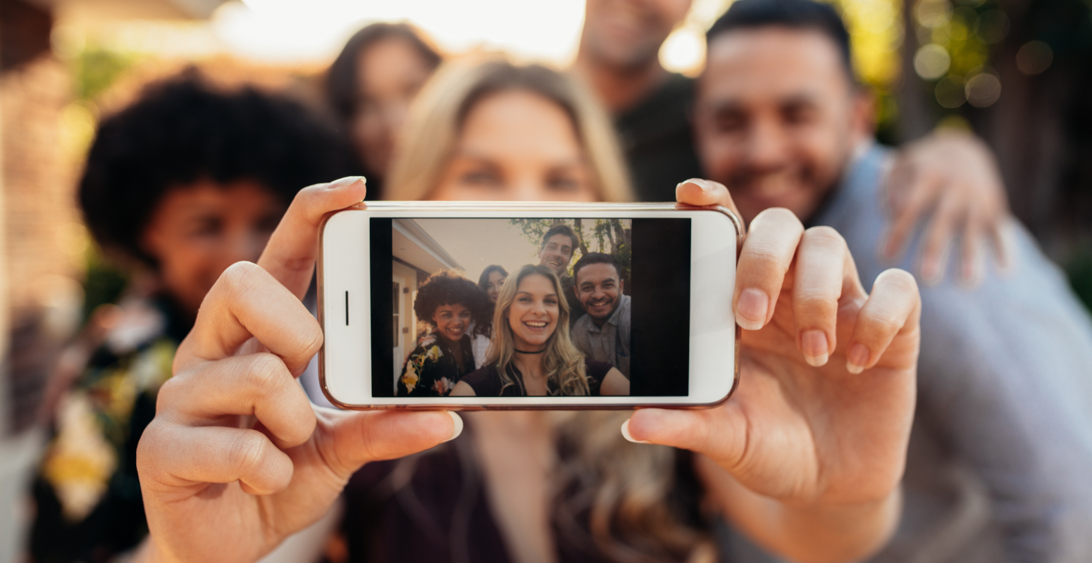 A group of friends taking a selfie together outdoors, capturing a happy moment on a smartphone screen, symbolizing social sharing and digital engagement.