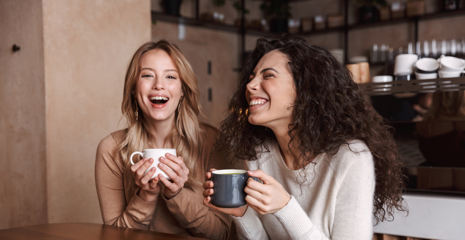 Two friends laughing and enjoying coffee, representing genuine connections in a secure referral programme safeguarded by Soreto's advanced anti-fraud tools