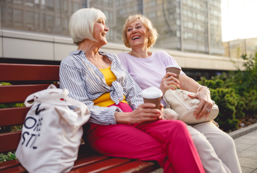 Two elderly women enjoying a coffee together on a bench